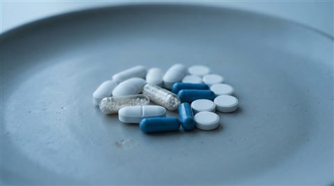 Photorealistic photo of pills and capsules, centered subject with a simple uncluttered composition, cool blue tones, quiet atmosphere, 16:9 aspect ratio