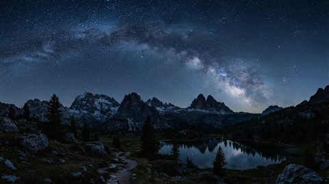 Photorealistic photo of milky way over mountains, wide shot with open space at the top for text, cool blue tones, quiet atmosphere, 16:9 aspect ratio