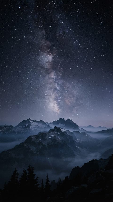 Cinematic film still of milky way over mountains, wide shot with open space at the top for text, misty morning haze, dreamy, 9:16 aspect ratio