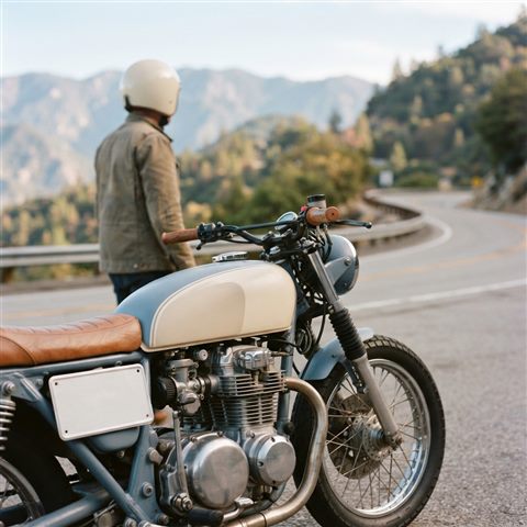 Photorealistic photo of a motorcycle on a mountain road, close-up detail with shallow depth of field, soft pastel colors, bright and cozy, 1:1 aspect ratio