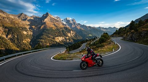 Photorealistic photo of a motorcycle on a mountain road, wide shot with open space at the top for text, vivid colors, high contrast, energetic, 16:9 aspect ratio