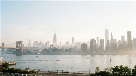 Photorealistic photo of the New York City skyline, wide shot with open space at the top for text, misty morning haze, dreamy, 16:9 aspect ratio