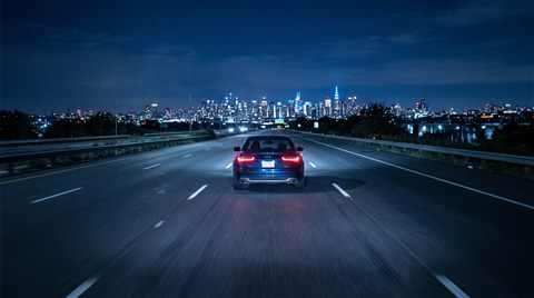 Photorealistic photo of car driving on an empty highway at night with city lights, centered subject with a simple uncluttered composition, cool blue tones, quiet atmosphere, 16:9 aspect ratio