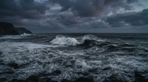 Photorealistic photo of ocean waves, wide shot with open space at the top for text, moody dark tones, dramatic lighting, 16:9 aspect ratio