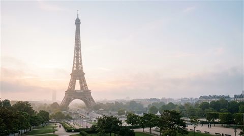 Photorealistic photo of the Eiffel Tower in Paris, wide shot with open space at the top for text, misty morning haze, dreamy, 16:9 aspect ratio