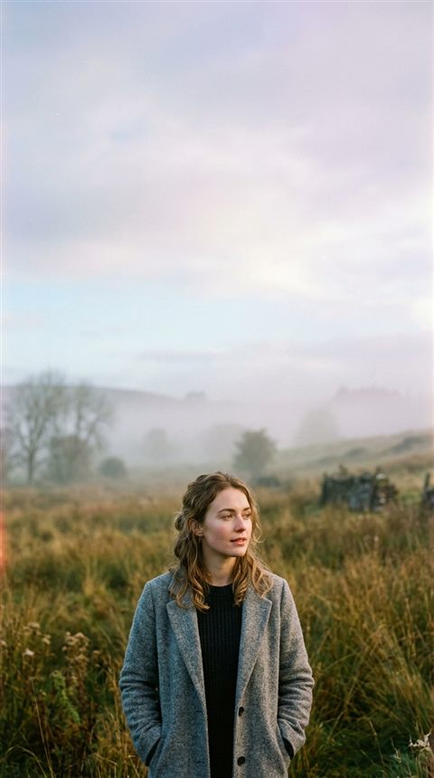 Cinematic film still of portrait of a fictional person with a natural expression, wide shot with open space at the top for text, misty morning haze, dreamy, 9:16 aspect ratio