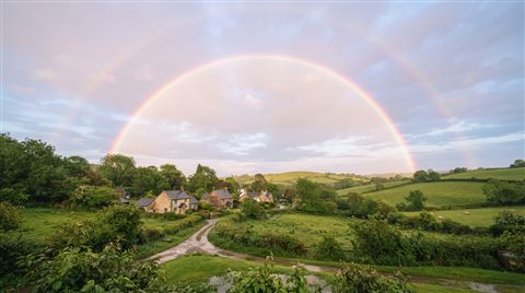 Photorealistic photo of rainbow after the rain, centered subject with a simple uncluttered composition, soft pastel colors, bright and cozy, 16:9 aspect ratio