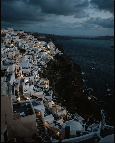Cinematic film still of white houses of Santorini above the sea, high-angle view from above, moody dark tones, dramatic lighting, 4:5 aspect ratio