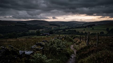 Photorealistic photo of peaceful countryside scenery with rolling hills, close-up detail with shallow depth of field, moody dark tones, dramatic lighting, 16:9 aspect ratio