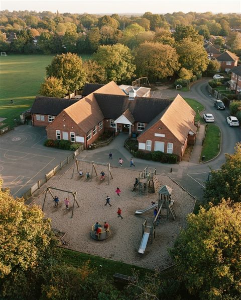 Cinematic film still of a school building with a playground, high-angle view from above, warm golden light, calm mood, 4:5 aspect ratio