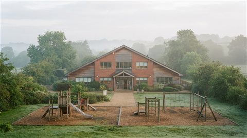 Photorealistic photo of a school building with a playground, centered subject with a simple uncluttered composition, misty morning haze, dreamy, 16:9 aspect ratio