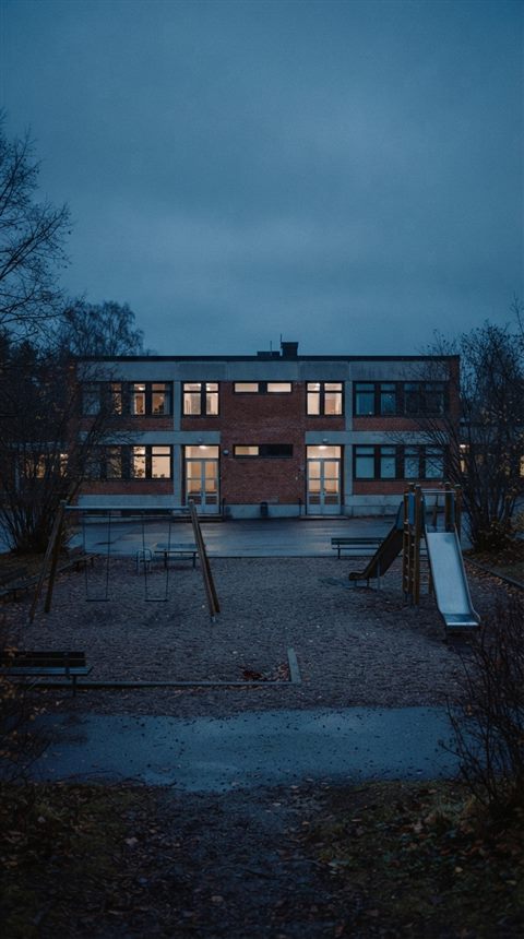 Cinematic film still of a school building with a playground, centered subject with a simple uncluttered composition, cool blue tones, quiet atmosphere, 9:16 aspect ratio
