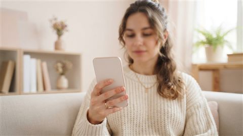 Photorealistic photo of smartphone in hand, wide shot with open space at the top for text, soft pastel colors, bright and cozy, 16:9 aspect ratio