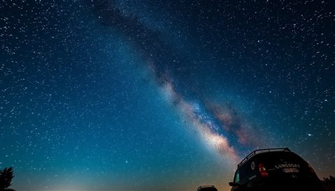 Photorealistic photo of Vibrant Milky Way galaxy stretching across a deep blue night sky filled with countless bright stars, centered subject with a simple uncluttered composition, warm golden light, calm mood, 16:9 aspect ratio