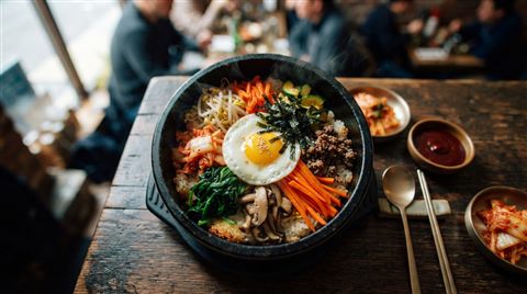 Cinematic film still of a colorful bibimbap in a stone pot with vegetables and an egg, high-angle view from above, vivid colors, high contrast, energetic, 16:9 aspect ratio