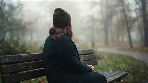 Cinematic film still of person sitting alone on a park bench seen from behind, close-up detail with shallow depth of field, misty morning haze, dreamy, 16:9 aspect ratio