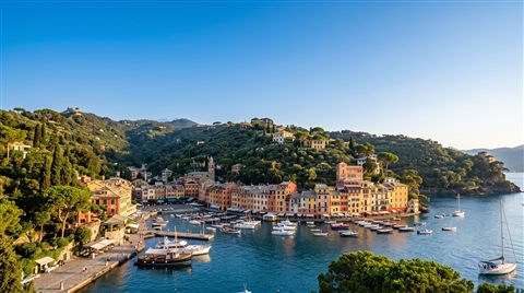 Photorealistic photo of small seaside town under a clear blue summer sky, wide shot with open space at the top for text, warm golden light, calm mood, 16:9 aspect ratio