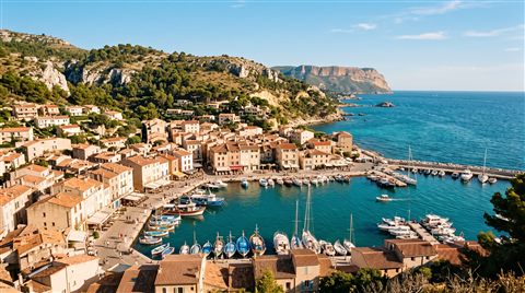 Cinematic film still of small seaside town under a clear blue summer sky, high-angle view from above, warm golden light, calm mood, 16:9 aspect ratio