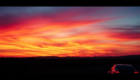 Cinematic film still of A vibrant evening horizon with brilliant gradients of orange, pink, and purple clouds over a calm silhouette landscape., close-up detail with shallow depth of field, vivid colors, high contrast, energetic, 16:9 aspect ratio