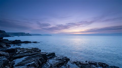 Photorealistic photo of sunset over the sea, wide shot with open space at the top for text, cool blue tones, quiet atmosphere, 16:9 aspect ratio