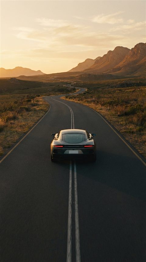 Cinematic film still of sleek generic sports car on an empty road, no brand badges, centered subject with a simple uncluttered composition, warm golden light, calm mood, 9:16 aspect ratio