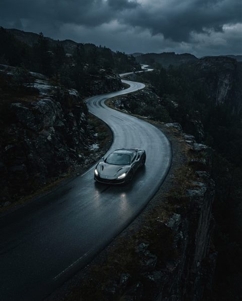 Cinematic film still of sleek generic sports car on an empty road, no brand badges, high-angle view from above, moody dark tones, dramatic lighting, 4:5 aspect ratio