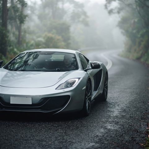 Photorealistic photo of sleek generic sports car on an empty road, no brand badges, close-up detail with shallow depth of field, misty morning haze, dreamy, 1:1 aspect ratio