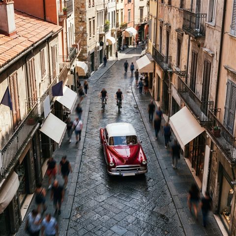 Photorealistic photo of generic vintage classic car on an old city street, no brand badges, high-angle view from above, vivid colors, high contrast, energetic, 1:1 aspect ratio