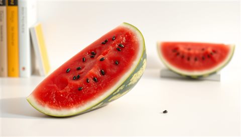 깨끗한 흰색 배경 위에 놓인 검은 씨가 박힌 선명한 붉은색 수박 조각, 사실적인 사진, 단순하고 깔끔한 구도 가운데 놓인 피사체, 따뜻한 황금빛, 차분한 분위기, 16:9 비율