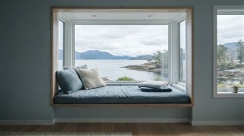Photorealistic photo of a window seat with cushions and a view, centered subject with a simple uncluttered composition, cool blue tones, quiet atmosphere, 16:9 aspect ratio